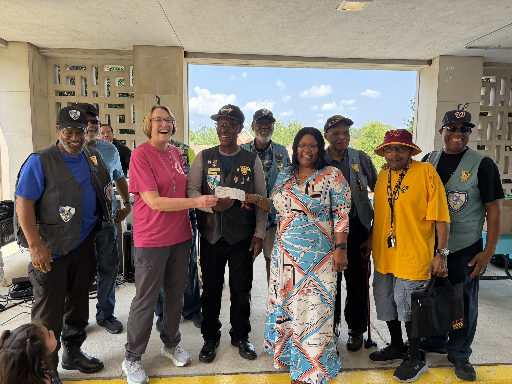 Photo of two women receiving a check from a group of volunteers directly outside St. Ann's Center.